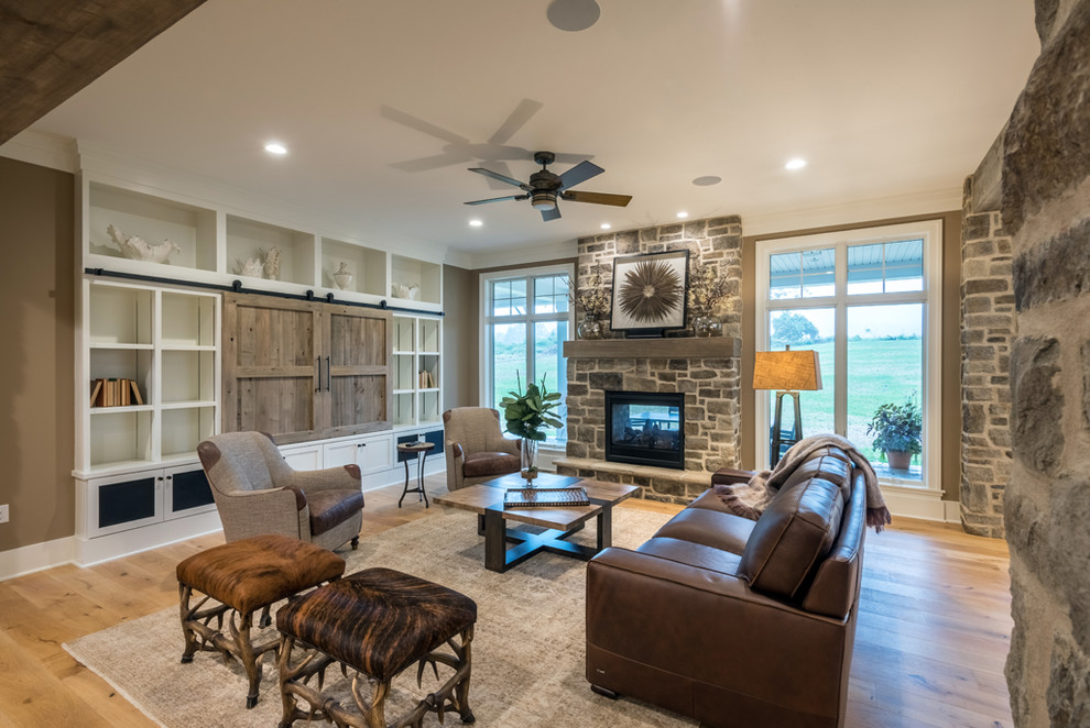 Photo of a mid-sized arts and crafts open concept family room in Other with beige walls, light hardwood floors, a two-sided fireplace, a stone fireplace surround, a built-in media wall and brown floor.