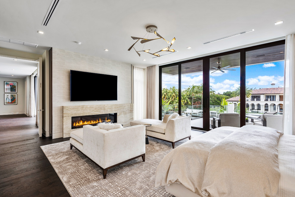 Large modern master bedroom in Miami with beige walls, medium hardwood floors, a ribbon fireplace, a stone fireplace surround and brown floor.