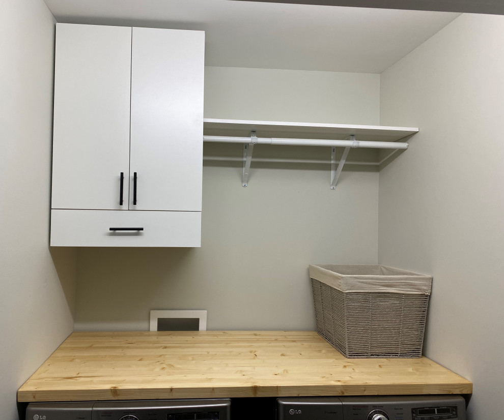Photo of a small eclectic single-wall laundry cupboard in Charlotte with flat-panel cabinets, white cabinets, wood benchtops, grey walls and a side-by-side washer and dryer.