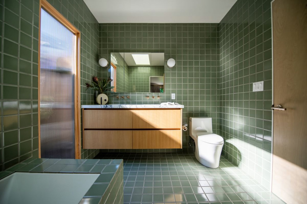 This is an example of a large midcentury ensuite bathroom in Los Angeles with light wood cabinets, a corner bath, a one-piece toilet, green tiles, ceramic tiles, green walls, ceramic flooring, a built-in sink, marble worktops, green floors, white worktops, double sinks and a floating vanity unit.
