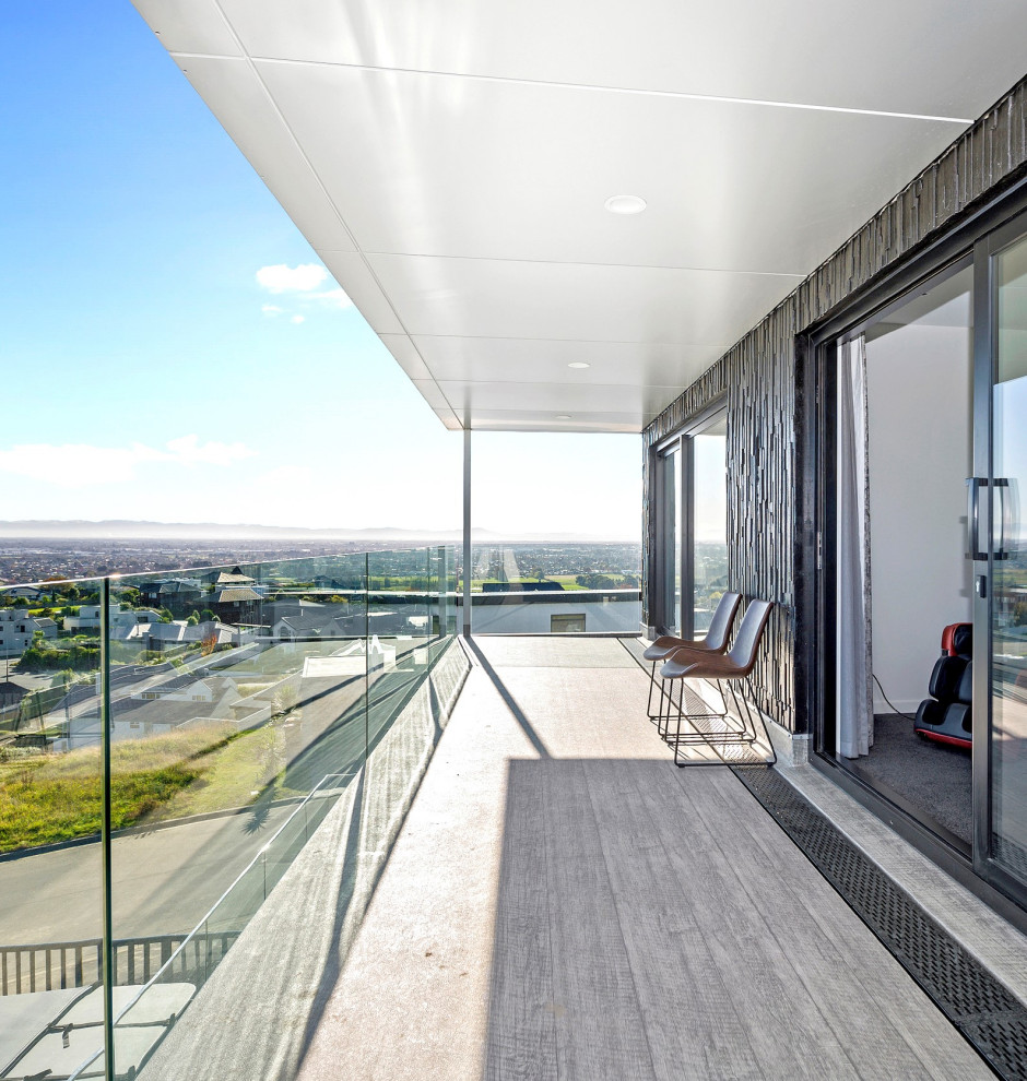 Design ideas for a large modern balcony in Christchurch with a roof extension and glass railing.