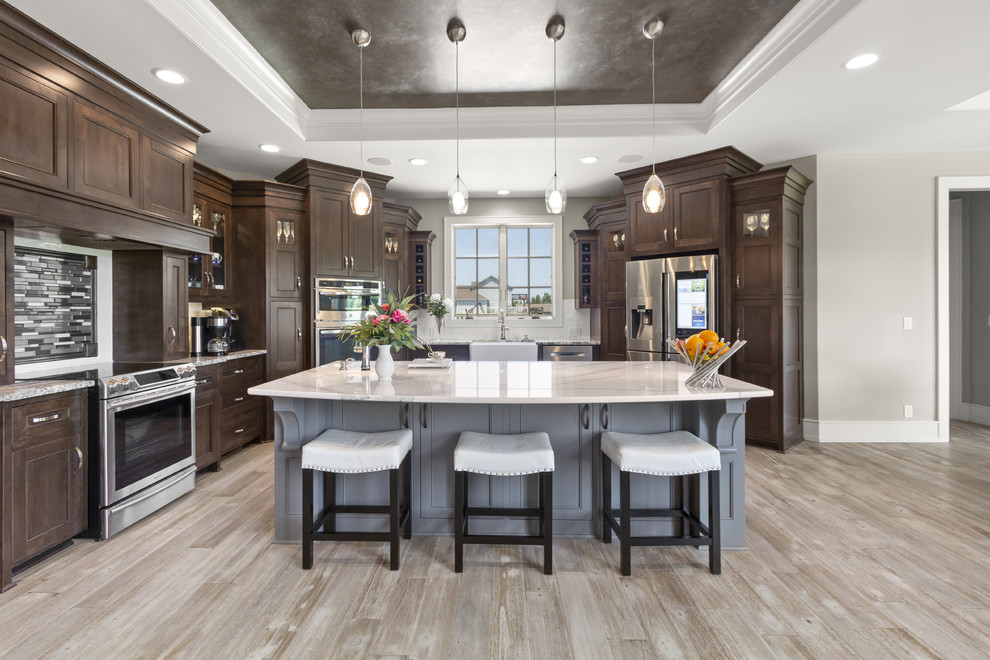 Inspiration for a transitional l-shaped kitchen in Other with a farmhouse sink, recessed-panel cabinets, dark wood cabinets, stainless steel appliances, light hardwood floors, with island, beige floor and beige benchtop.