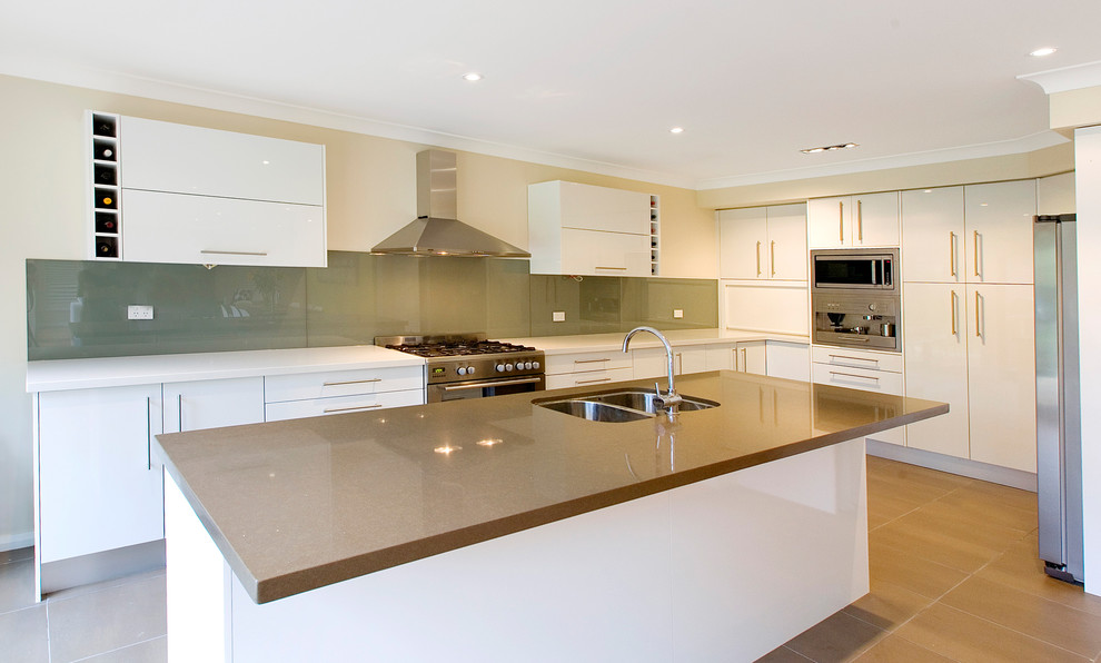 This is an example of a large contemporary u-shaped open plan kitchen in Sydney with an undermount sink, flat-panel cabinets, white cabinets, quartz benchtops, grey splashback, glass sheet splashback, white appliances, porcelain floors and with island.