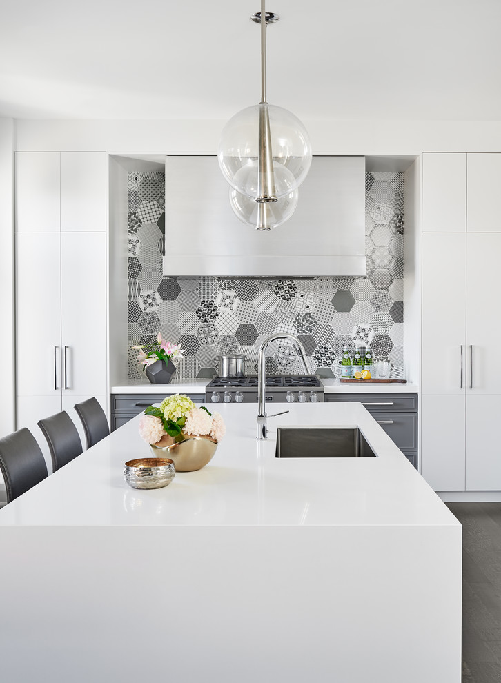 This is an example of a mid-sized contemporary l-shaped open plan kitchen in Toronto with an undermount sink, flat-panel cabinets, white cabinets, quartz benchtops, multi-coloured splashback, porcelain splashback, stainless steel appliances, dark hardwood floors, with island and brown floor.