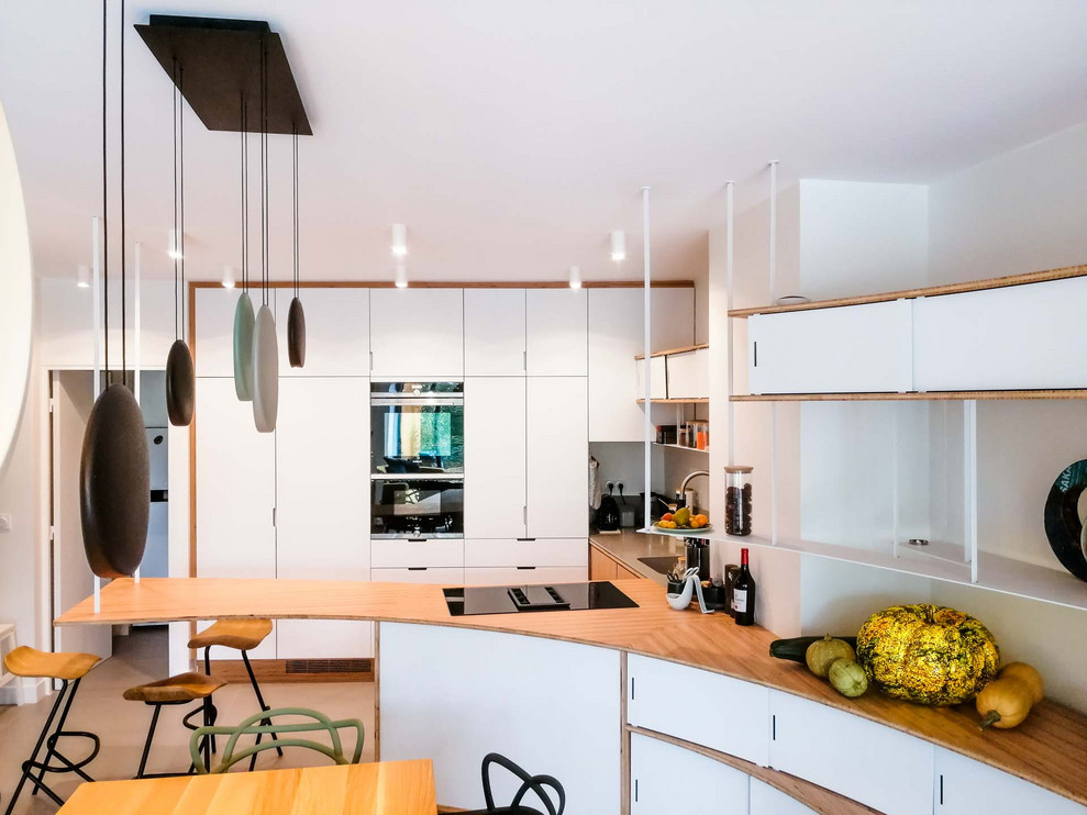 Photo of an expansive contemporary u-shaped open plan kitchen in Paris with an undermount sink, beaded inset cabinets, white cabinets, wood benchtops, grey splashback, black appliances, ceramic floors, a peninsula, grey floor and beige benchtop.