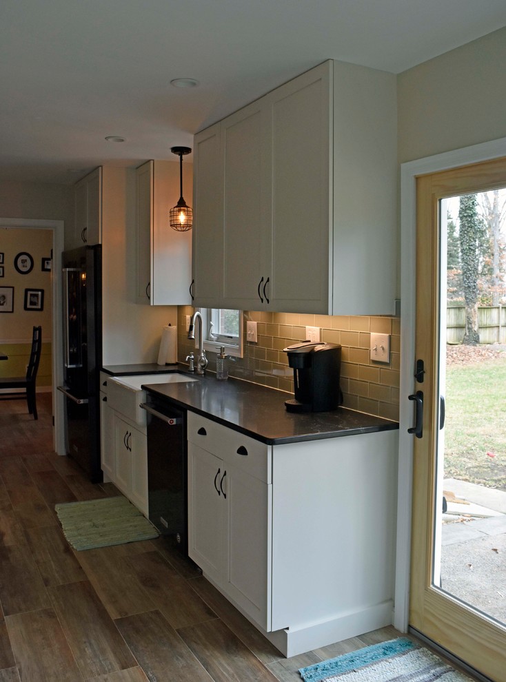 Enclosed kitchen - mid-sized transitional galley laminate floor and brown floor enclosed kitchen idea in DC Metro with a farmhouse sink, shaker cabinets, white cabinets, granite countertops, gray backsplash, subway tile backsplash, stainless steel appliances, no island and black countertops