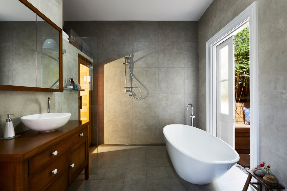Large eclectic bathroom in Sydney with furniture-like cabinets, dark wood cabinets, a freestanding tub, an open shower, a wall-mount toilet, gray tile, porcelain tile, grey walls, porcelain floors, with a sauna, a vessel sink, wood benchtops, grey floor and an open shower.