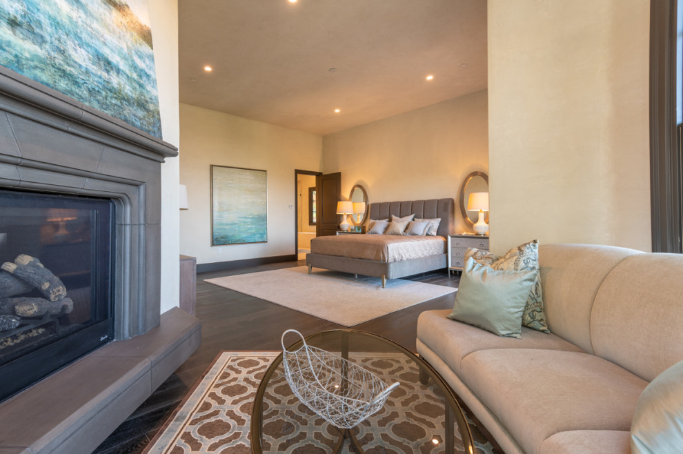 Expansive master bedroom in Other with beige walls, dark hardwood flooring, a standard fireplace, a stone fireplace surround and brown floors.