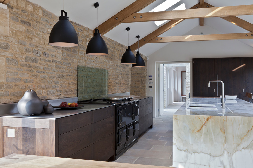 Contemporary galley kitchen in London with an undermount sink, flat-panel cabinets, dark wood cabinets, glass sheet splashback, with island, marble benchtops and black appliances.