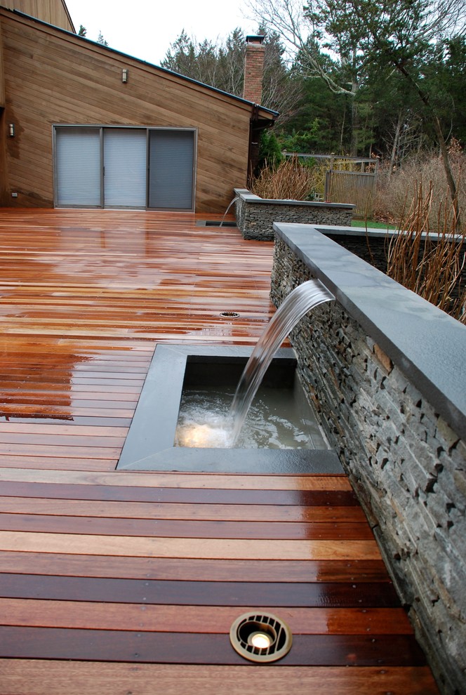 Photo of a large beach style backyard deck in New York with a water feature and a roof extension.