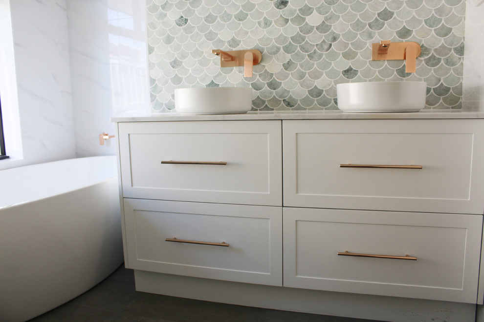 Photo of a mid-sized contemporary kids bathroom in Perth with flat-panel cabinets, white cabinets, a freestanding tub, a corner shower, white tile, porcelain tile, white walls, porcelain floors, a vessel sink, marble benchtops, grey floor, a hinged shower door and grey benchtops.