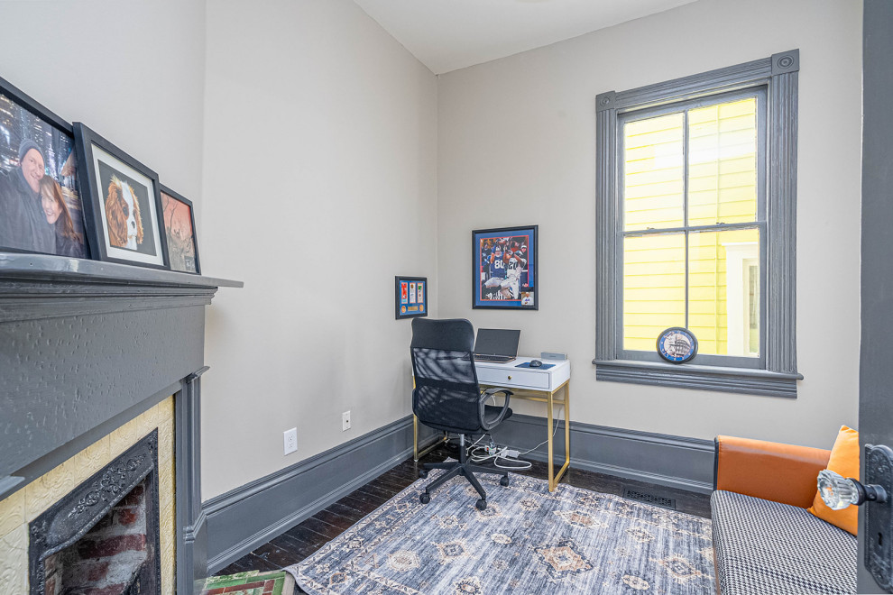 Exempel på ett litet klassiskt arbetsrum, med vita väggar, mörkt trägolv, en öppen hörnspis, en spiselkrans i trä, ett fristående skrivbord och svart golv