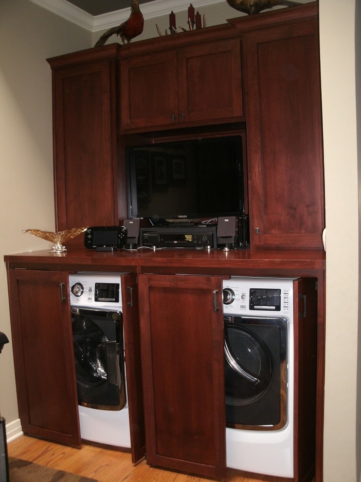 This is an example of a mid-sized arts and crafts galley utility room in Los Angeles with recessed-panel cabinets, dark wood cabinets, solid surface benchtops, beige walls, light hardwood floors and a concealed washer and dryer.