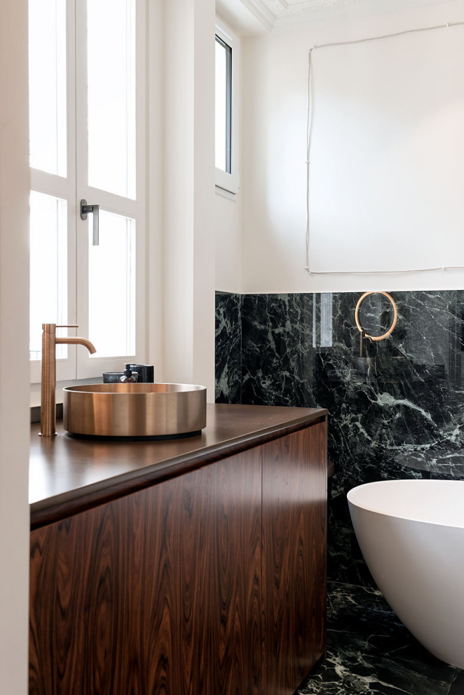 Cette photo montre une salle de bain tendance en bois foncé avec un placard à porte plane, une baignoire indépendante, un carrelage noir, un mur blanc, une vasque, un plan de toilette en bois, un sol noir, un plan de toilette marron, meuble simple vasque et meuble-lavabo encastré.