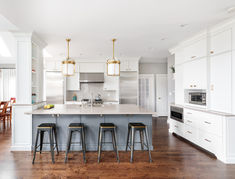 Inspiration for a mid-sized transitional l-shaped open plan kitchen in Chicago with recessed-panel cabinets, white cabinets, grey splashback, subway tile splashback, stainless steel appliances, medium hardwood floors and with island.