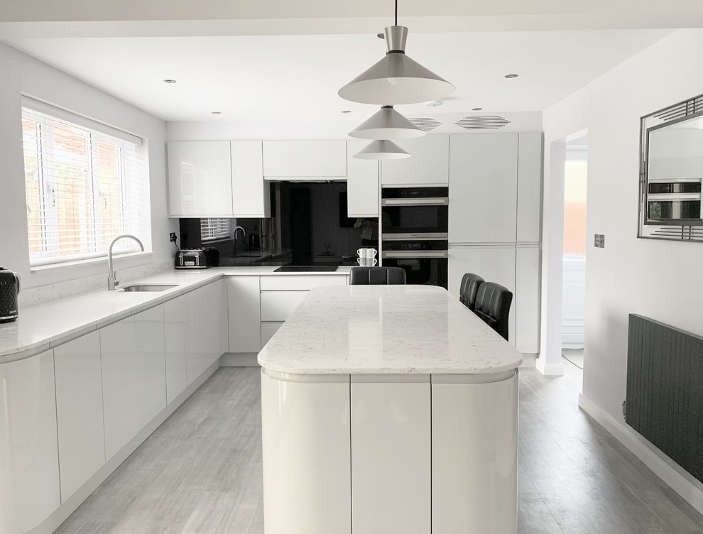 Inspiration for a mid-sized modern l-shaped eat-in kitchen in Other with an undermount sink, flat-panel cabinets, grey cabinets, quartzite benchtops, black splashback, glass sheet splashback, black appliances, laminate floors, with island, grey floor and white benchtop.