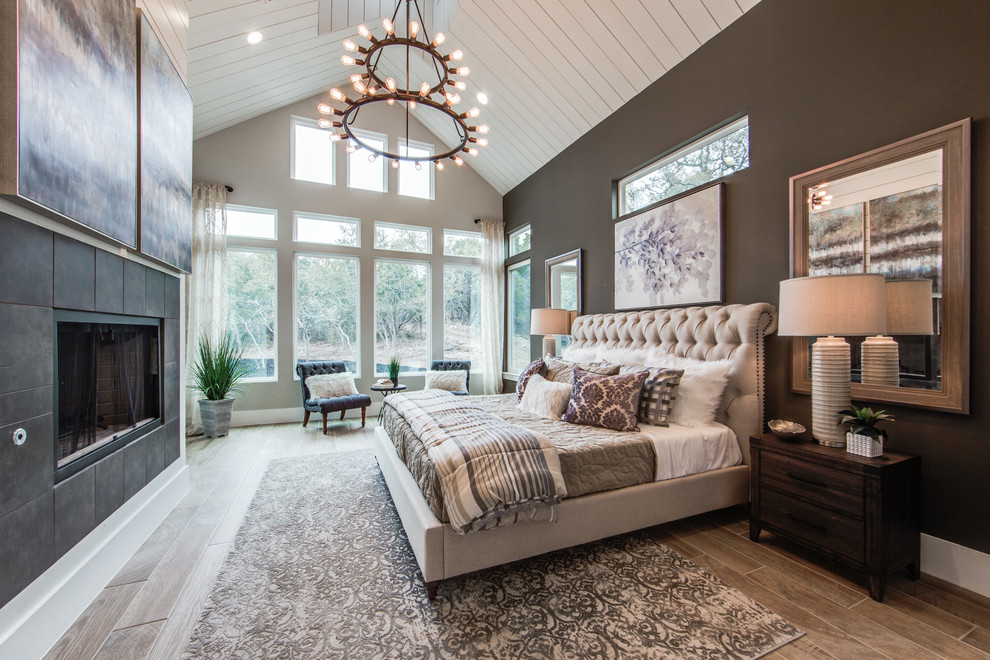 Inspiration for a large country master bedroom in Dallas with grey walls, porcelain floors, a standard fireplace, a tile fireplace surround and brown floor.