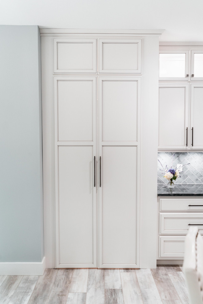 Huge transitional l-shaped laminate floor, gray floor and tray ceiling open concept kitchen photo with an undermount sink, flat-panel cabinets, white cabinets, quartz countertops, gray backsplash, ceramic backsplash, black appliances and an island