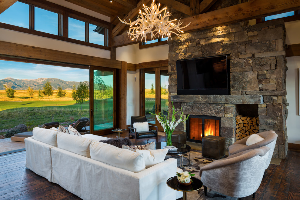 Photo of a large country open concept family room in Other with white walls, dark hardwood floors, a standard fireplace, a stone fireplace surround, a wall-mounted tv and brown floor.