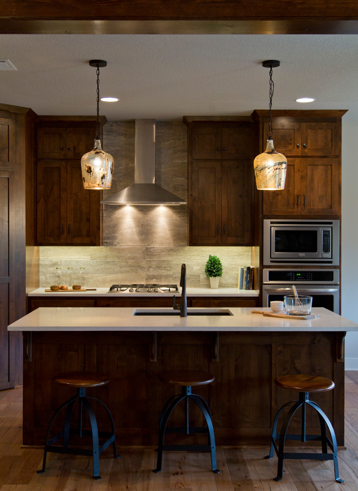 Inspiration for a large country l-shaped open plan kitchen in Kansas City with an undermount sink, recessed-panel cabinets, dark wood cabinets, beige splashback, stone tile splashback, stainless steel appliances, medium hardwood floors, with island and brown floor.