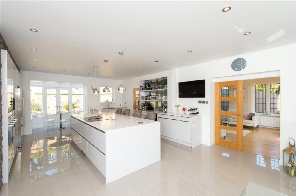 This is an example of a large contemporary grey and white galley open plan kitchen in Other with a single-bowl sink, flat-panel cabinets, white cabinets, quartz worktops, metallic splashback, mirror splashback, stainless steel appliances, porcelain flooring, an island, white floors, white worktops and a feature wall.