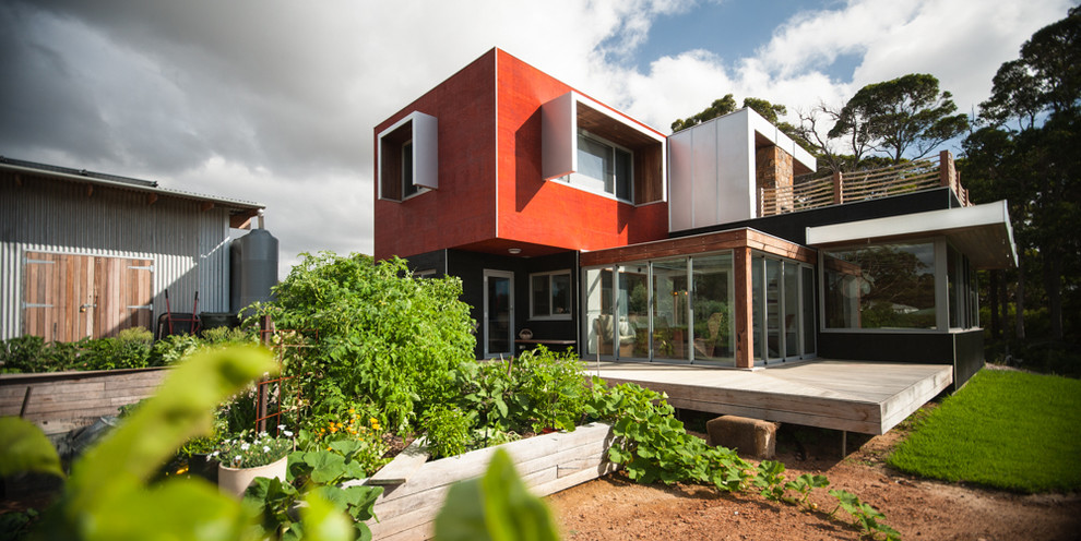 Photo of a small contemporary two-storey red exterior in Other with wood siding and a flat roof.