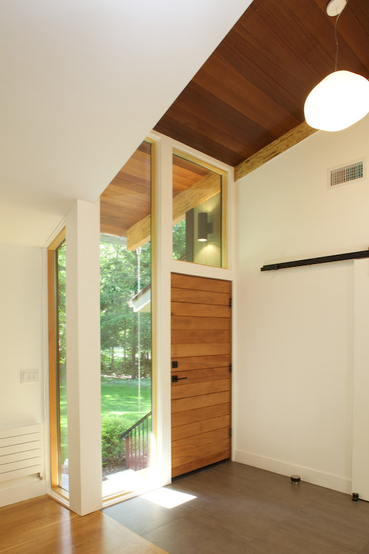 Inspiration for a mid-sized midcentury foyer in Bridgeport with white walls, porcelain floors, a single front door, a medium wood front door and brown floor.