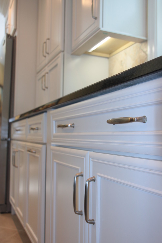 Mid-sized transitional l-shaped vinyl floor eat-in kitchen photo with an undermount sink, recessed-panel cabinets, white cabinets, beige backsplash, stone tile backsplash, stainless steel appliances and an island