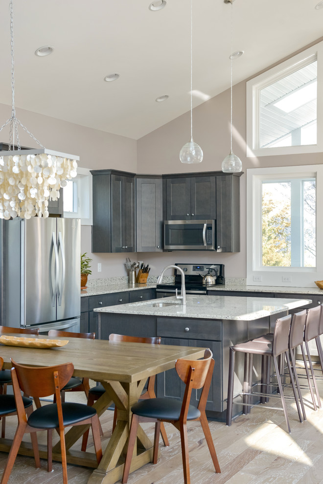 Example of a mid-sized transitional l-shaped light wood floor and brown floor open concept kitchen design with an undermount sink, shaker cabinets, gray cabinets, granite countertops, stainless steel appliances, an island and gray countertops
