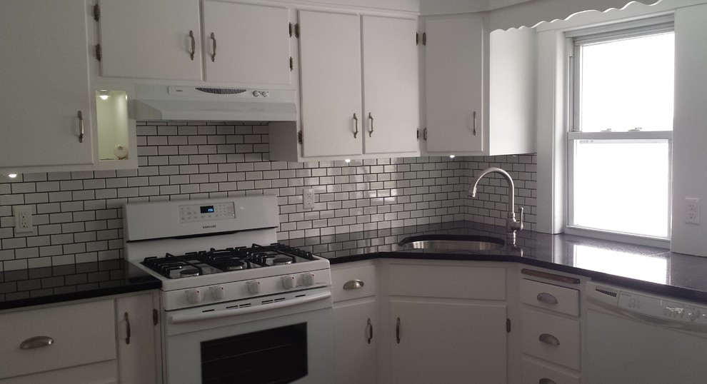 Mid-sized elegant u-shaped light wood floor enclosed kitchen photo in Boston with an undermount sink, flat-panel cabinets, white cabinets, granite countertops, white backsplash, subway tile backsplash, white appliances and no island
