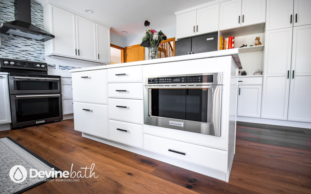 Open concept kitchen - large transitional l-shaped medium tone wood floor open concept kitchen idea in Portland with an undermount sink, recessed-panel cabinets, white cabinets, quartz countertops, white backsplash, glass tile backsplash, stainless steel appliances, an island and white countertops