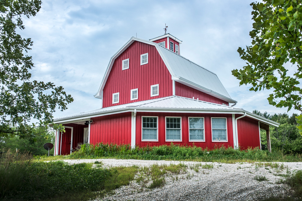 This is an example of a mid-sized country three-storey red house exterior in Omaha with metal siding and a gambrel roof.