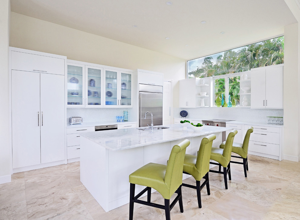This is an example of a large tropical l-shaped open plan kitchen in Miami with a double-bowl sink, flat-panel cabinets, white cabinets, quartzite benchtops, white splashback, ceramic splashback, stainless steel appliances, marble floors, with island and beige floor.