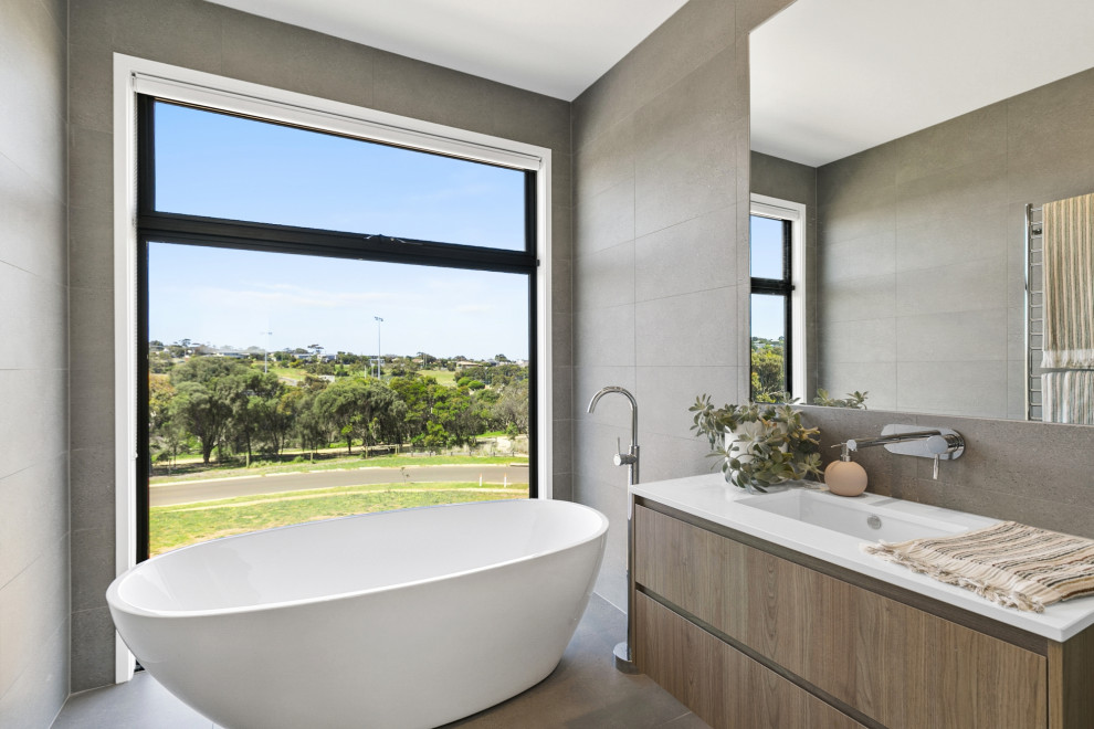 Design ideas for a mid-sized contemporary master bathroom in Geelong with flat-panel cabinets, light wood cabinets, a freestanding tub, porcelain floors, a drop-in sink, solid surface benchtops and grey floor.