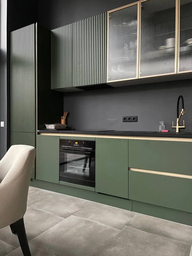 Inspiration for a mid-sized contemporary single-wall open plan kitchen in Moscow with a drop-in sink, flat-panel cabinets, green cabinets, solid surface benchtops, black splashback, black appliances, porcelain floors, no island, beige floor and black benchtop.