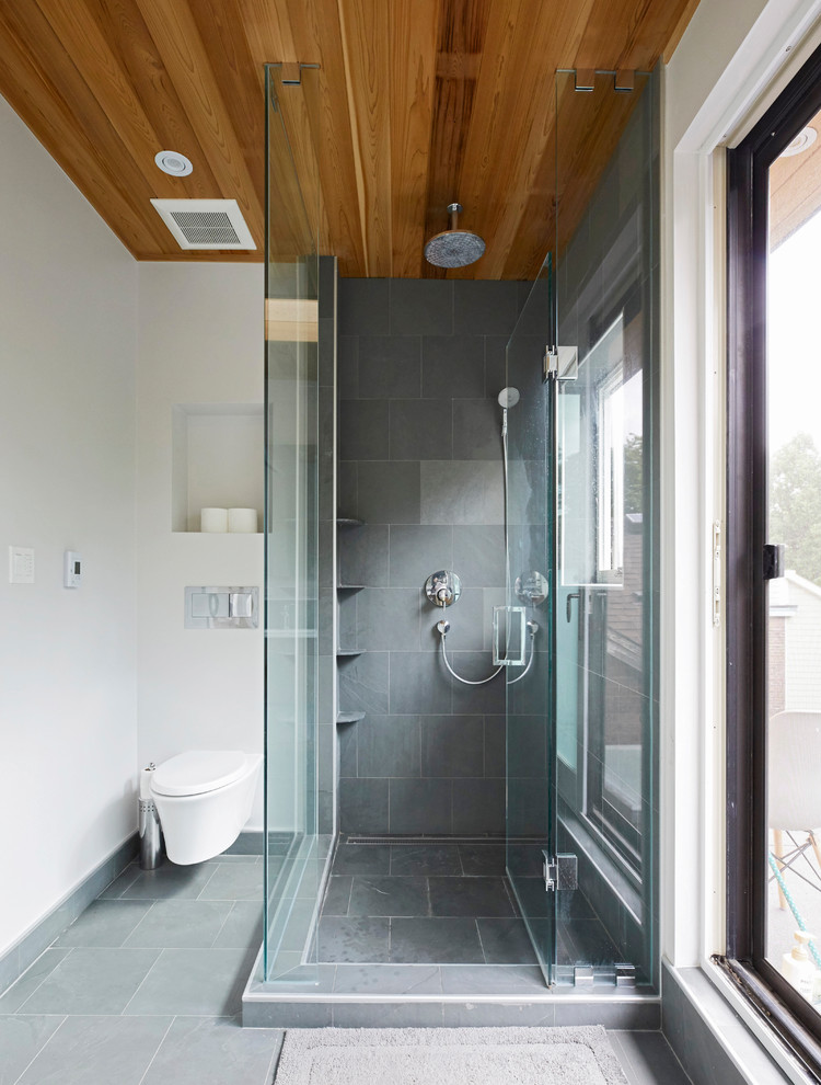 Photo of a mid-sized modern master bathroom in Toronto with flat-panel cabinets, medium wood cabinets, a corner shower, a wall-mount toilet, gray tile, slate, white walls, slate floors, an undermount sink, solid surface benchtops, grey floor, a hinged shower door and white benchtops.