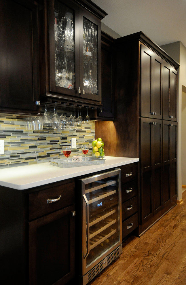 This is an example of a large transitional l-shaped eat-in kitchen in Minneapolis with an undermount sink, shaker cabinets, dark wood cabinets, quartz benchtops, multi-coloured splashback, glass tile splashback, stainless steel appliances, medium hardwood floors, with island, brown floor and yellow benchtop.