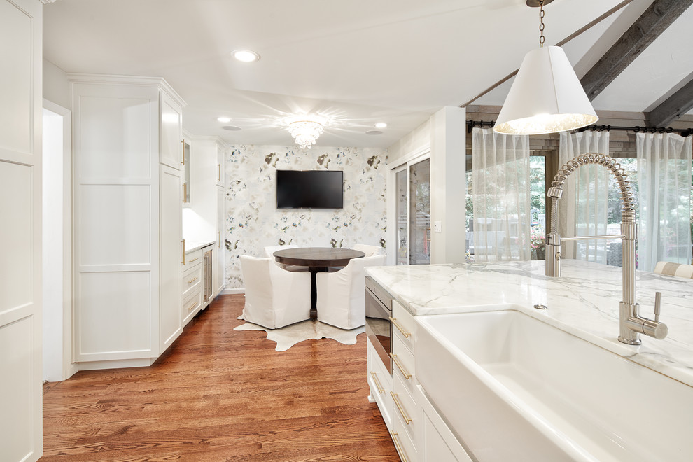 Inspiration for a large transitional u-shaped medium tone wood floor and brown floor eat-in kitchen remodel with a farmhouse sink, shaker cabinets, white cabinets, marble countertops, white backsplash, marble backsplash, stainless steel appliances and an island
