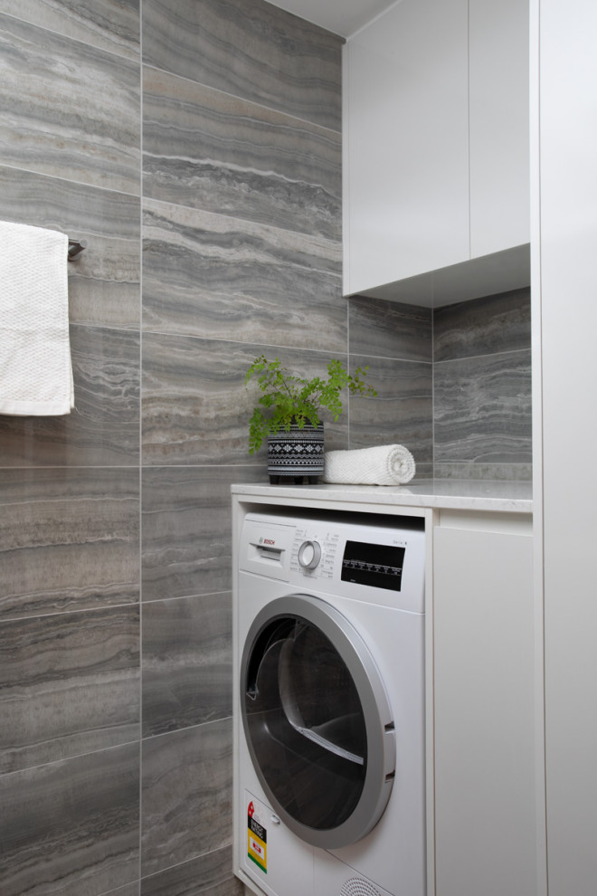 Small contemporary galley dedicated laundry room in Brisbane with white cabinets, grey walls, porcelain floors, grey floor and white benchtop.