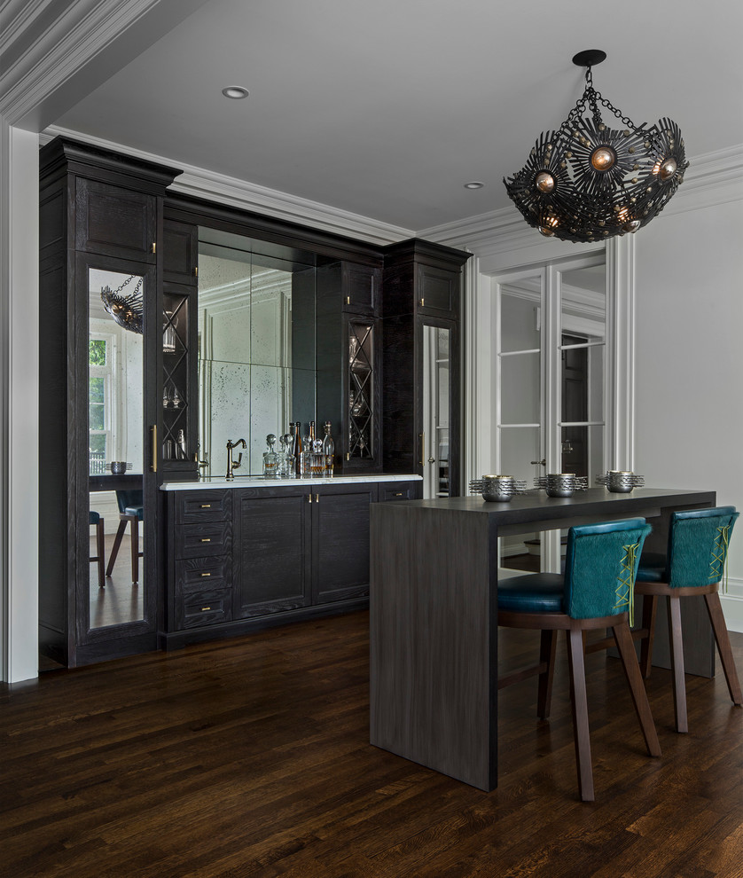 Design ideas for a mid-sized transitional galley seated home bar in Detroit with an undermount sink, dark wood cabinets, marble benchtops, dark hardwood floors, recessed-panel cabinets, mirror splashback, brown floor and white benchtop.