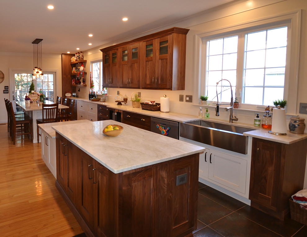 Expansive transitional l-shaped eat-in kitchen in Philadelphia with a farmhouse sink, raised-panel cabinets, medium wood cabinets, quartzite benchtops, grey splashback, subway tile splashback, stainless steel appliances, light hardwood floors, multiple islands, beige floor and white benchtop.