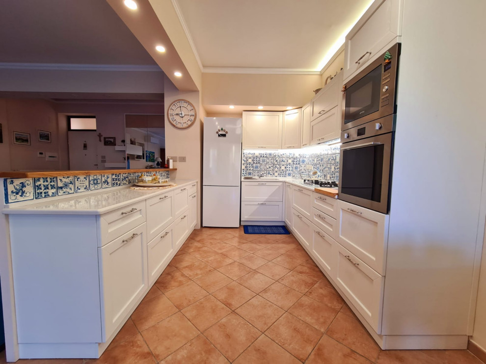 Photo of a medium sized country galley kitchen/diner in Catania-Palermo with a built-in sink, raised-panel cabinets, white cabinets, engineered stone countertops, blue splashback, ceramic splashback, stainless steel appliances, porcelain flooring, an island, multi-coloured floors, white worktops and a drop ceiling.