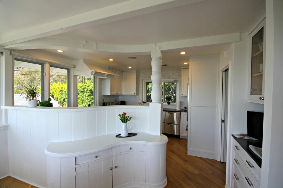 Photo of a mid-sized traditional u-shaped eat-in kitchen in Los Angeles with a farmhouse sink, shaker cabinets, white cabinets, grey splashback, stone tile splashback, stainless steel appliances, medium hardwood floors and no island.