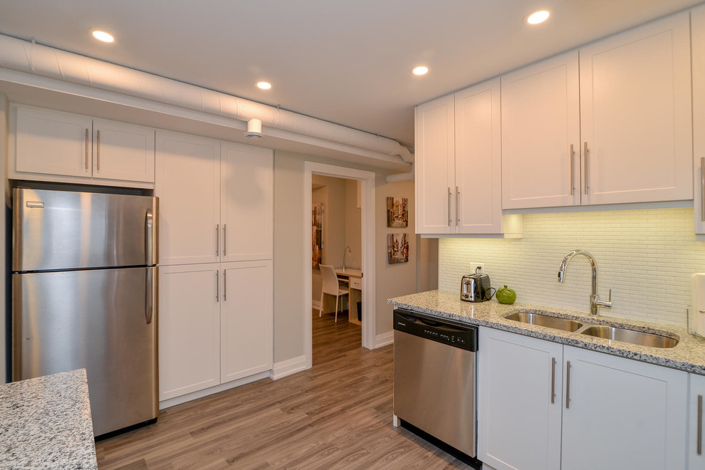 Example of a mid-sized transitional u-shaped medium tone wood floor and gray floor open concept kitchen design with an undermount sink, shaker cabinets, white cabinets, granite countertops, stainless steel appliances and a peninsula