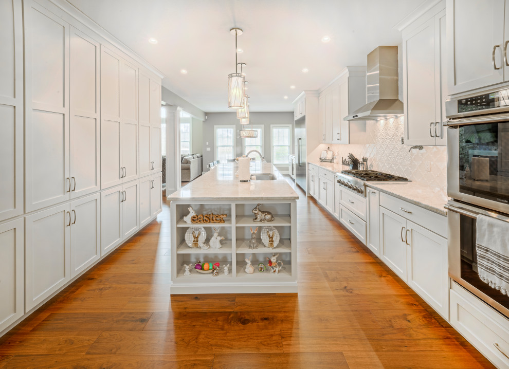 Inspiration for a large transitional u-shaped medium tone wood floor and brown floor kitchen pantry remodel with an undermount sink, shaker cabinets, white cabinets, granite countertops, white backsplash, ceramic backsplash, stainless steel appliances, an island and white countertops
