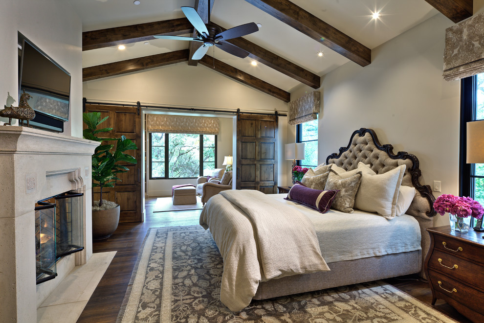 This is an example of a mediterranean master bedroom in Sacramento with grey walls, dark hardwood floors, a standard fireplace, a stone fireplace surround and brown floor.