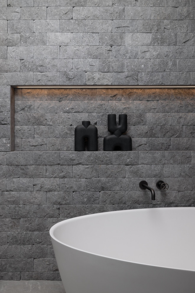 Bild på ett mellanstort industriellt svart svart badrum med dusch, med släta luckor, blå skåp, ett fristående badkar, en dusch i en alkov, en toalettstol med hel cisternkåpa, grå kakel, kakelplattor, bruna väggar, klinkergolv i porslin, ett fristående handfat, granitbänkskiva, grått golv och dusch med gångjärnsdörr