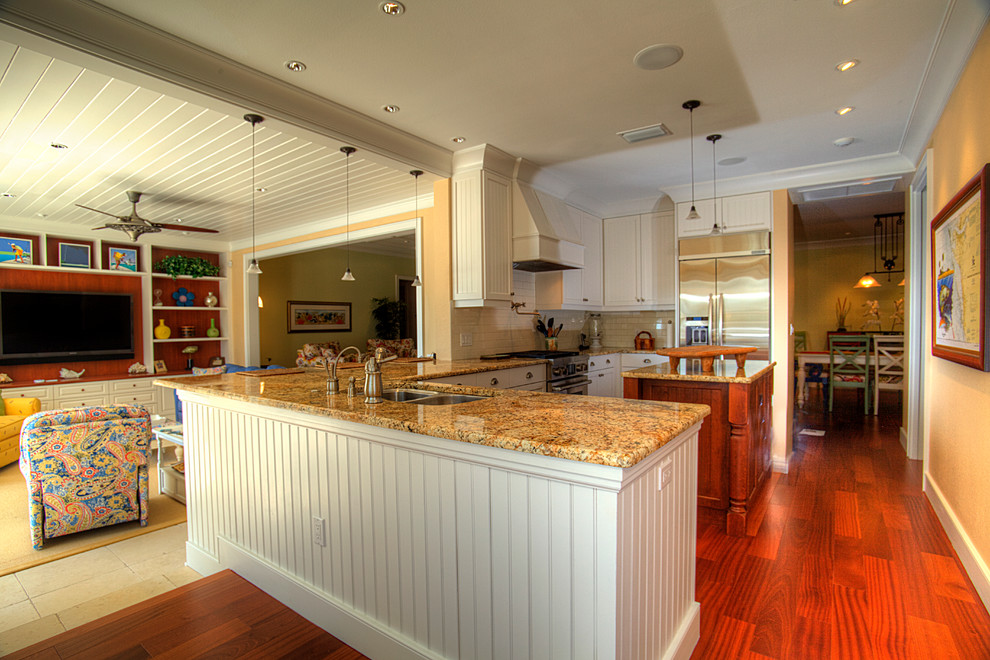 Inspiration for a large tropical u-shaped open plan kitchen in Tampa with a double-bowl sink, white cabinets, granite benchtops, white splashback, subway tile splashback, stainless steel appliances, dark hardwood floors and with island.