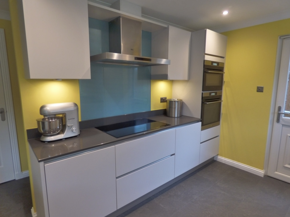 Inspiration for a mid-sized modern l-shaped open plan kitchen in Glasgow with an integrated sink, flat-panel cabinets, grey cabinets, quartzite benchtops, blue splashback, glass sheet splashback, panelled appliances, laminate floors, grey floor and grey benchtop.