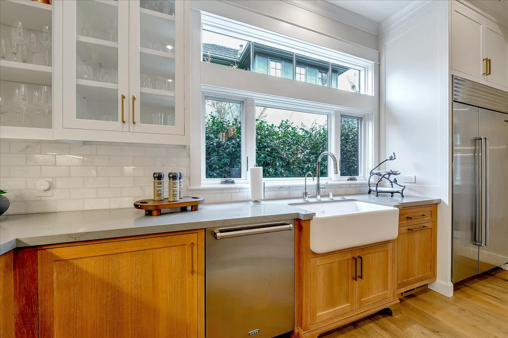 Bild på ett stort amerikanskt grå grått kök, med en rustik diskho, skåp i shakerstil, skåp i mellenmörkt trä, vitt stänkskydd, stänkskydd i tunnelbanekakel, rostfria vitvaror, mellanmörkt trägolv, en köksö och brunt golv